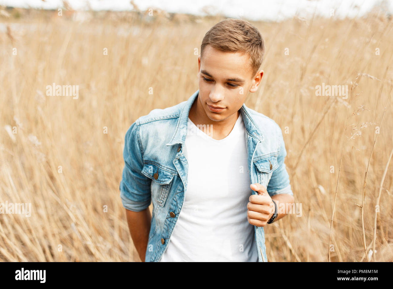Handsome young man in a jeans jacket and a white t-shirt in grass outdoors Stock Photo