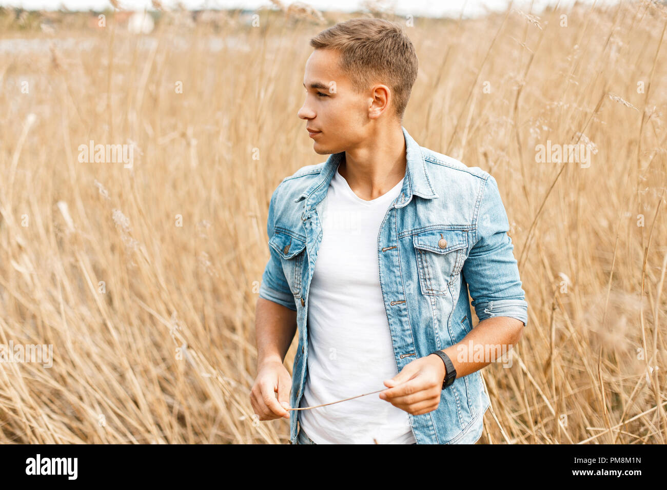 Handsome young guy in jeans clothes and a white T-shirt is walking outdoors in the grass Stock Photo