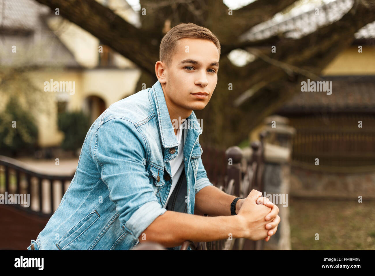 Handsome stylish man in jeans clothes and a white T-shirt near a house in the garden Stock Photo