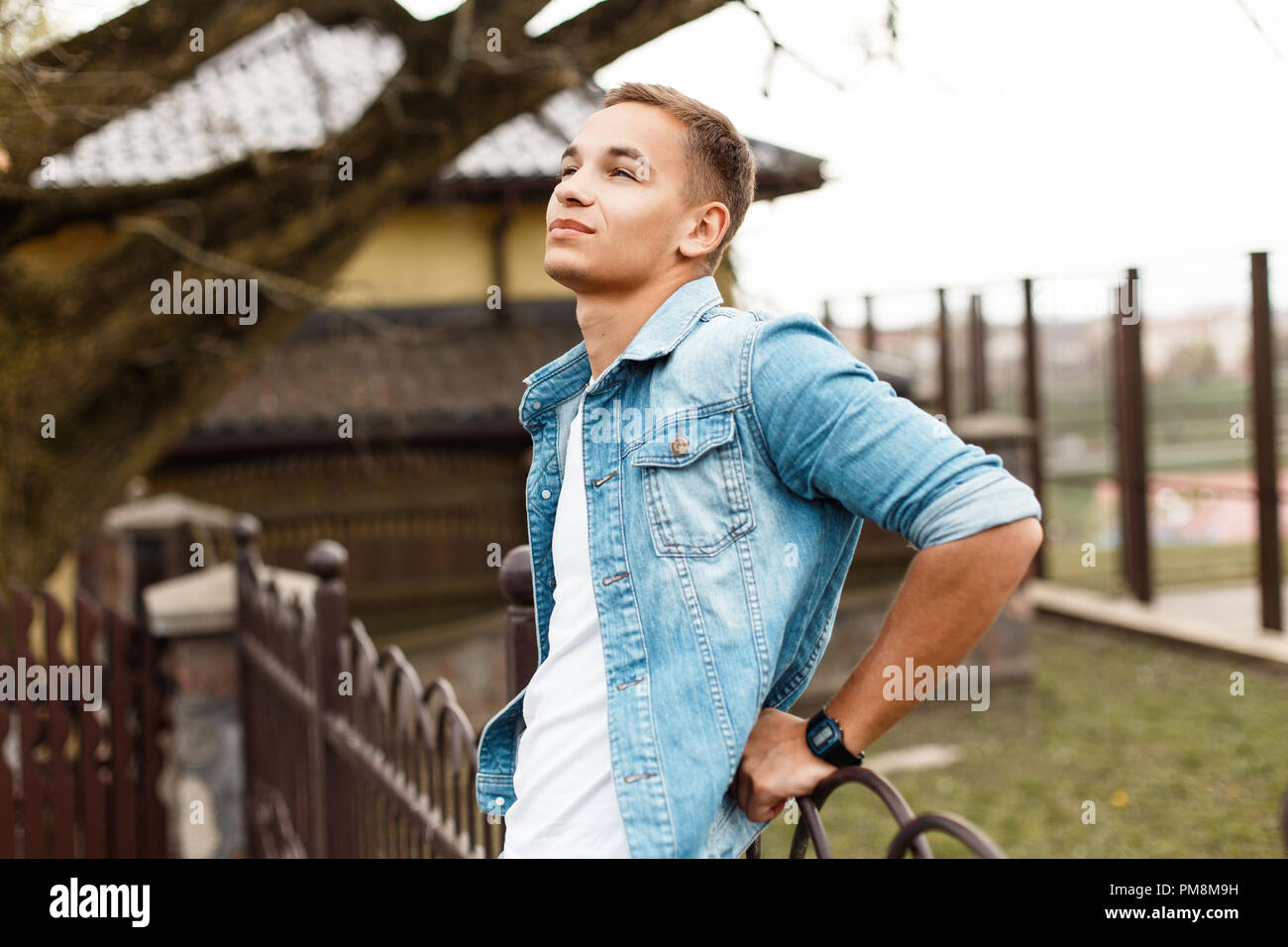 Handsome young stylish man in a jeans jacket and a white T-shirt is enjoying the moment and looking up Stock Photo