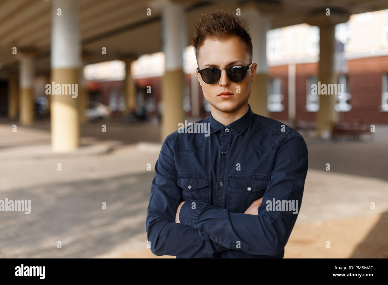 handsome man in sunglasses and a fashionable shirt posing on the street on a sunny day Stock Photo
