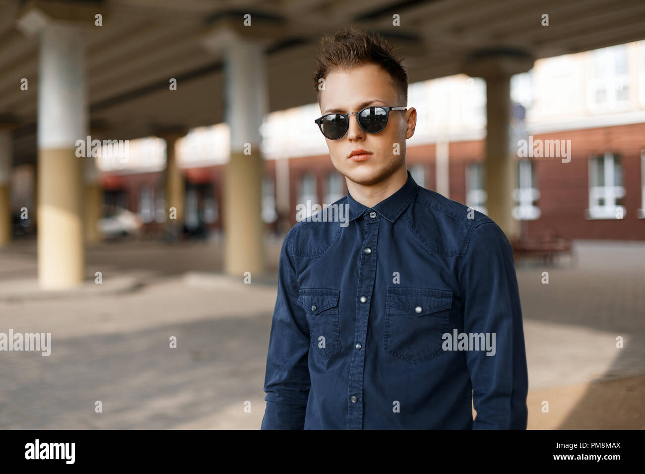 Young stylish handsome man in sunglasses and a blue shirt in a sunny day on the street Stock Photo