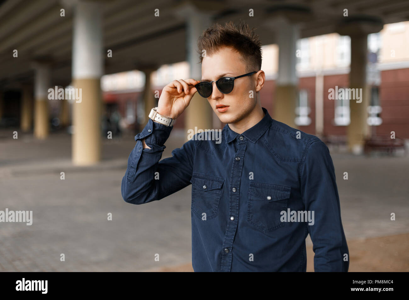 Handsome fashionable man in a blue shirt adjusts sunglasses on the street Stock Photo
