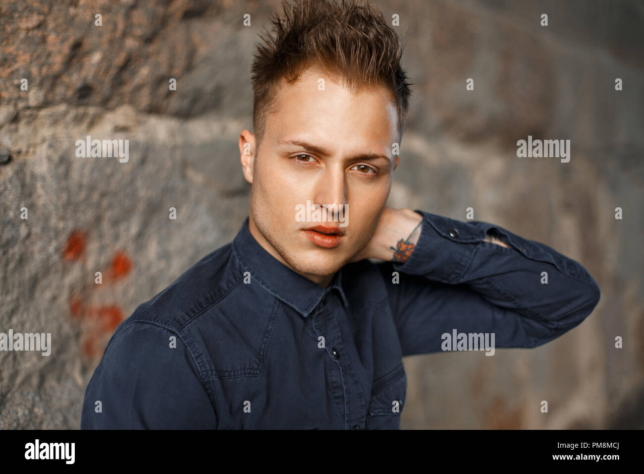 Close-up portrait of a handsome young man in a blue shirt near a stone wall Stock Photo