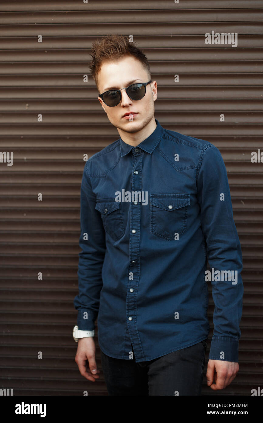 Stylish fashionable man in sunglasses and a shirt near a metal wall Stock Photo