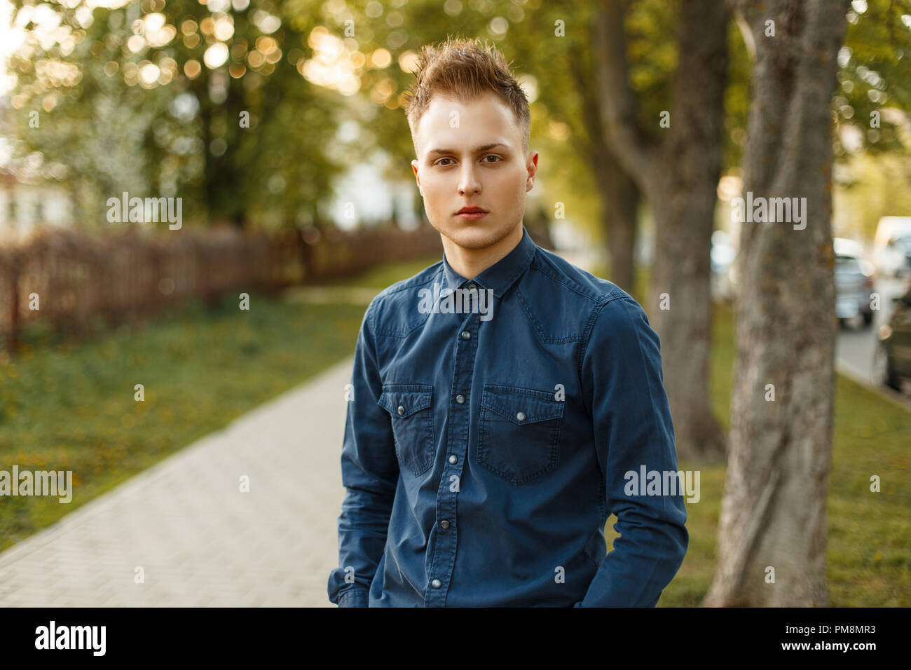 Young man in a blue shirt in the park on a spring sunny day Stock Photo