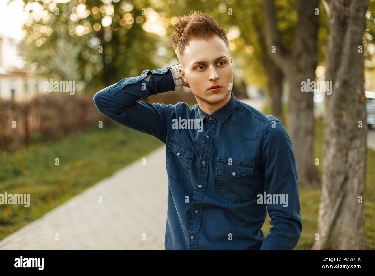 Handsome young stylish man in a blue shirt posing in the park on a sunny day Stock Photo