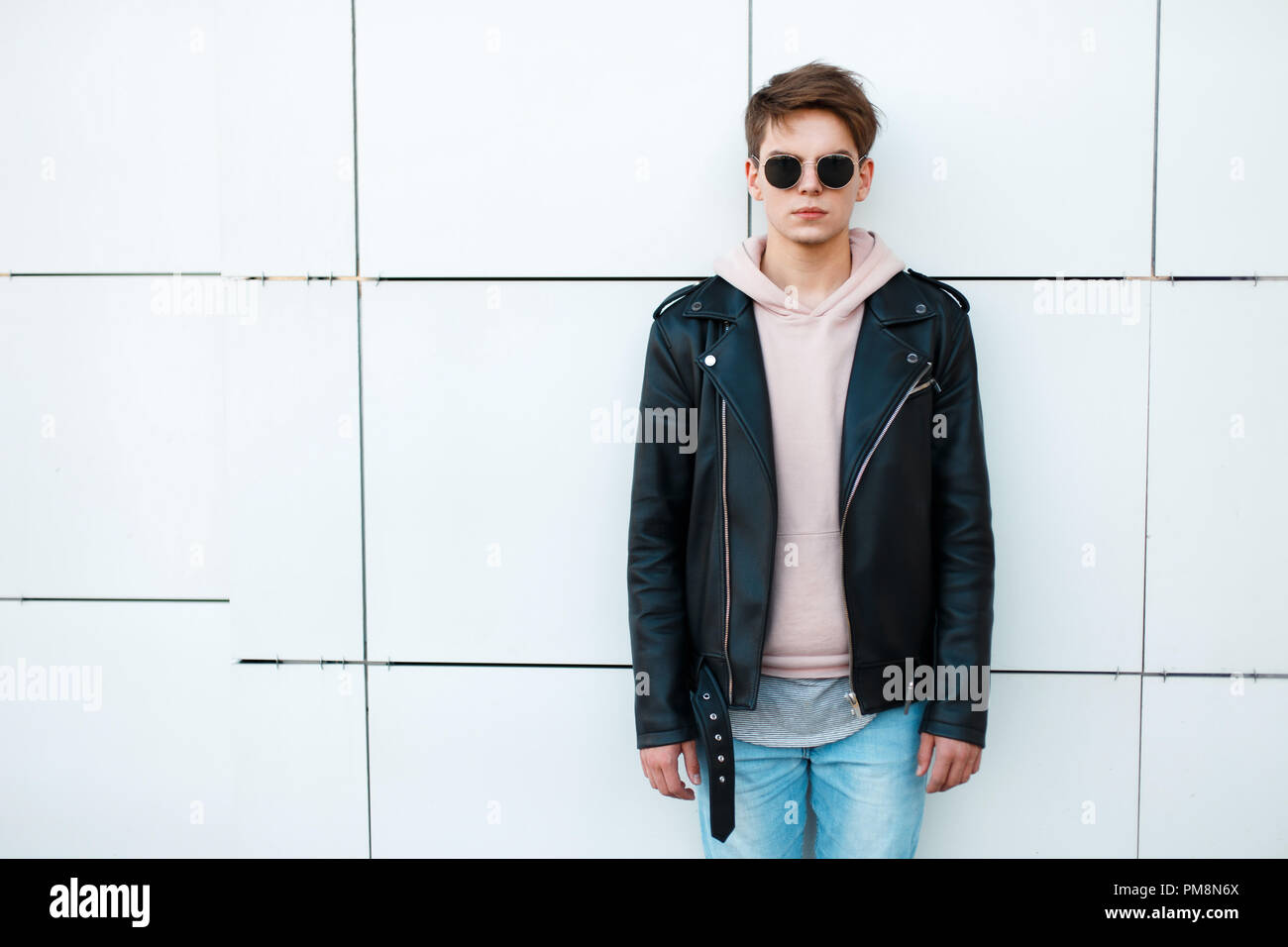 Young Man In A Black Leather Jacket And A Pink Sweatshirt Near A White 