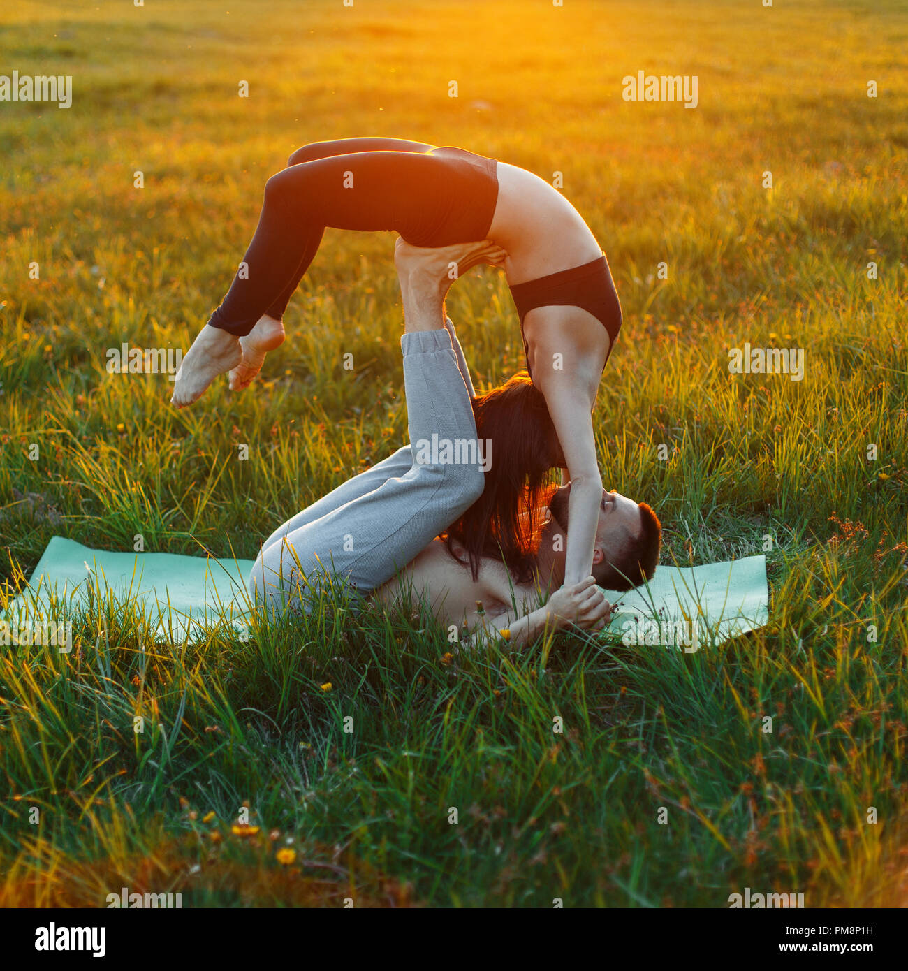 Young couple doing yoga outside the city on the grass at sunset Stock Photo