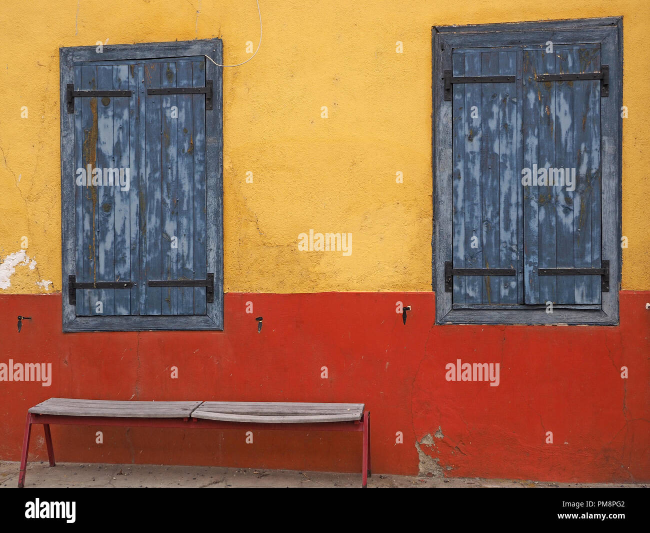 Rustic faded blue wooden window shutters in yellow and red wall of building in the Ariege Pyrennees, France make blocks of colour Stock Photo