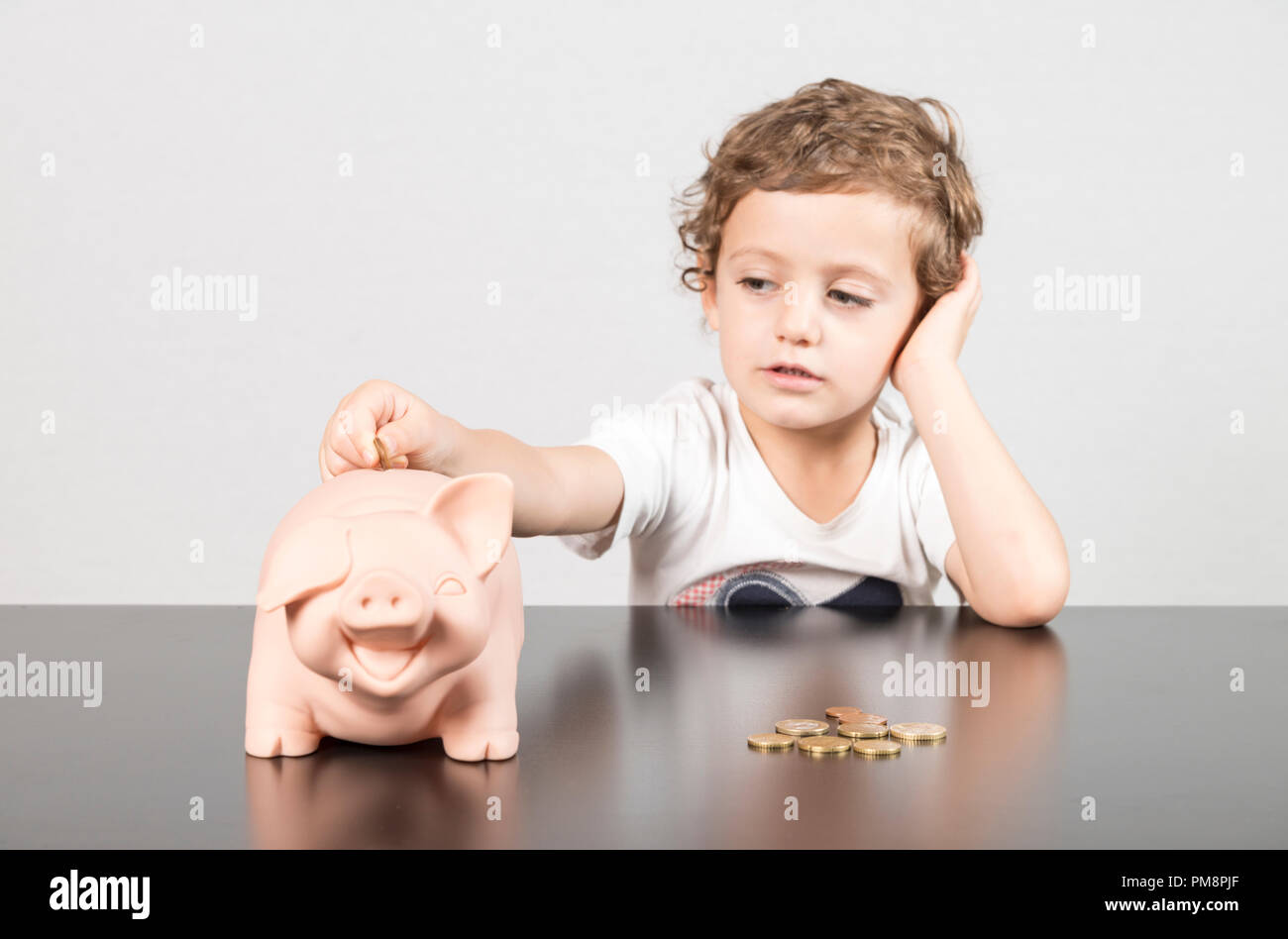 Child inserting coins in a piggy bank Stock Photo - Alamy