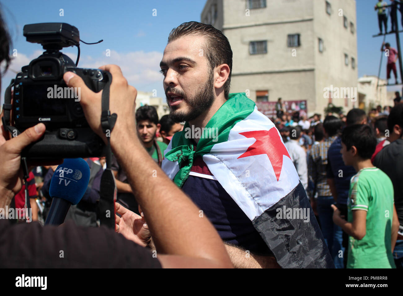 A man covered with the Syrian flag seen speaking to the media during the protest against the Syrian regime. Hundreds of protesters came out in Idlib city on with the slogan of no alternative to toppling the regime and the demonstrators chanting and cheering we are civilians and we want freedom and we don’t want the Syrian regime. Stock Photo