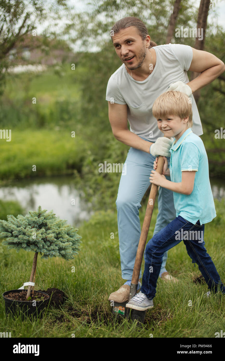 Smiling adult father and his son planting a tree outdoors in park Stock ...