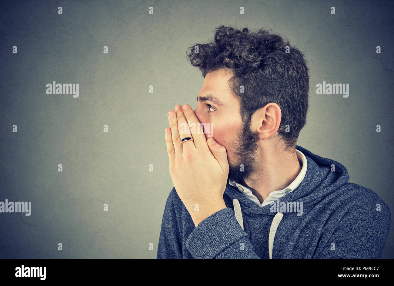 Young man covering mouth while gossiping and telling secrets in whisper. Stock Photo