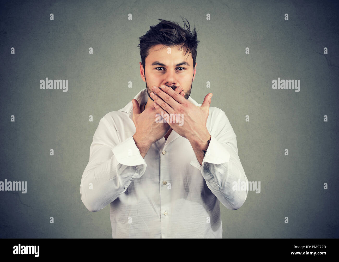 Young man in white shirt covering mouth keeping privacy and speaking no evil Stock Photo