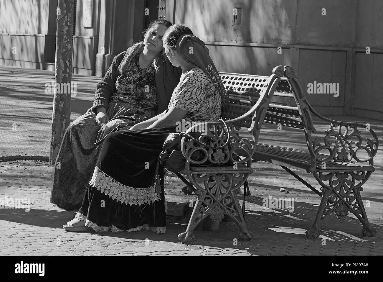 Women chat on a bench in Calle San Pablo, Sevilla, Andalusia, Spain: black and white version Stock Photo