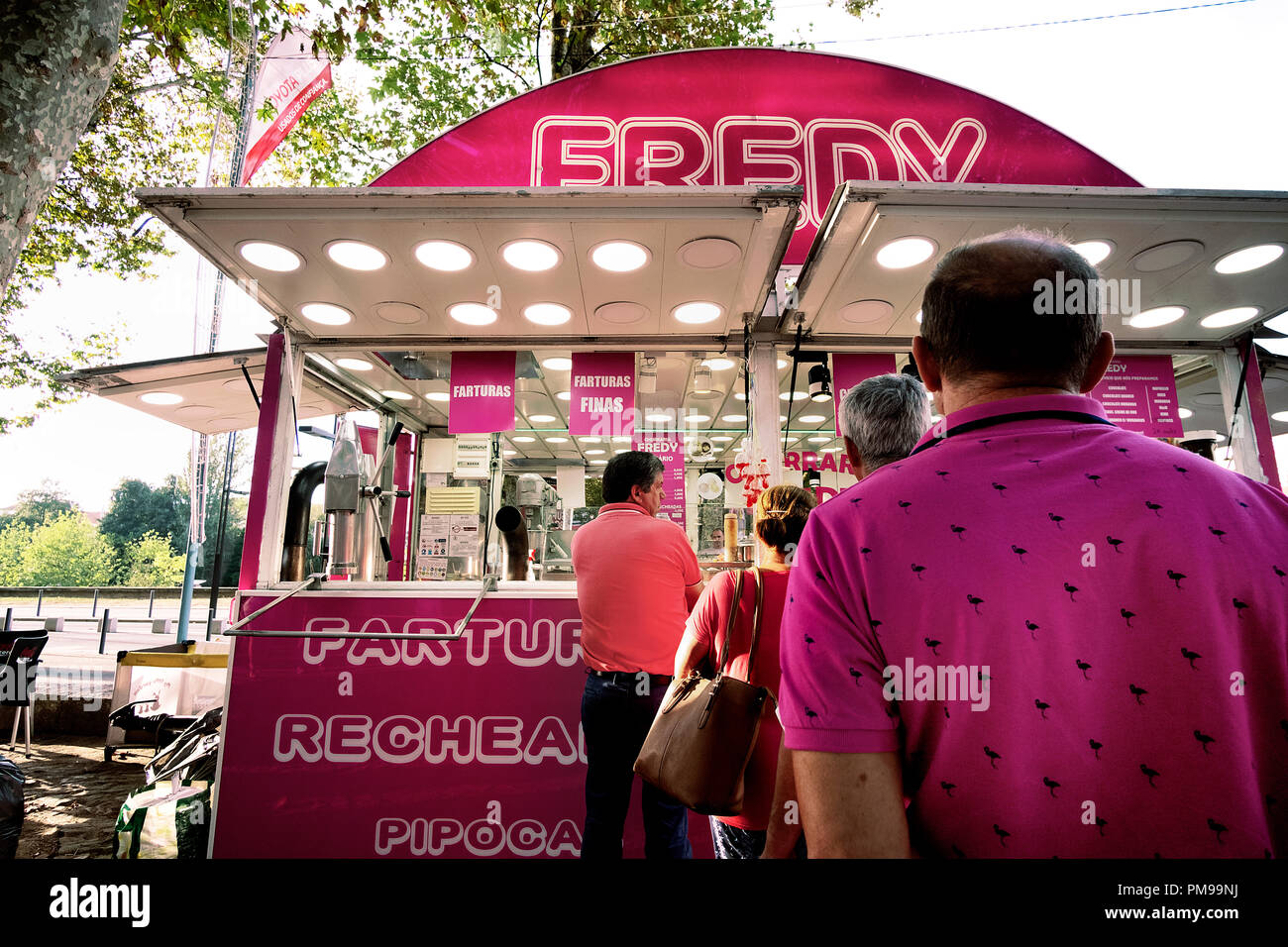 people line up for street food on a pink food trailer, in the line a guy with pink shirt Stock Photo