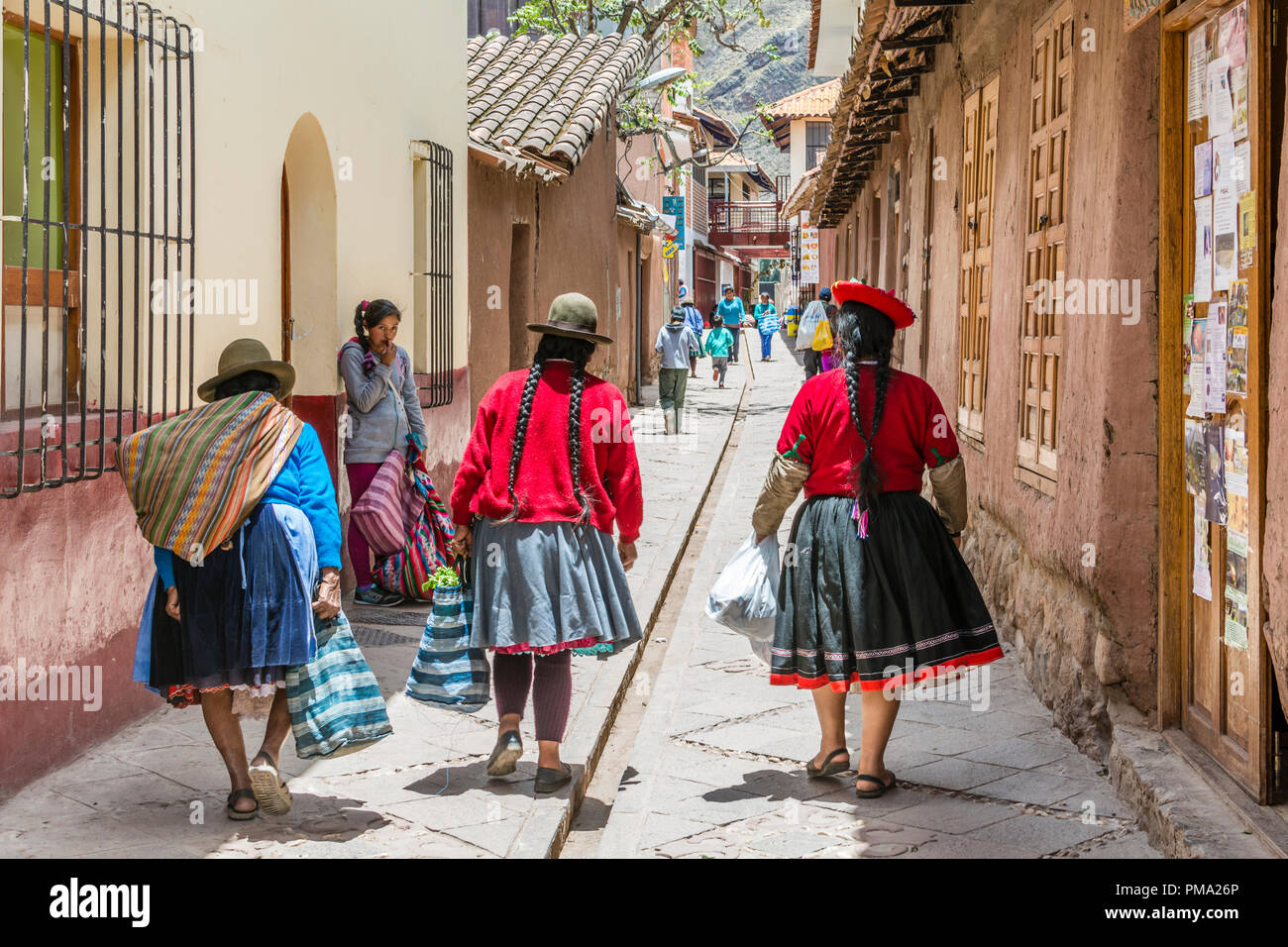 Pisac Peru, Peruvian women with braids wearing colorful clothing and hats walk down a narrow street. Stock Photo