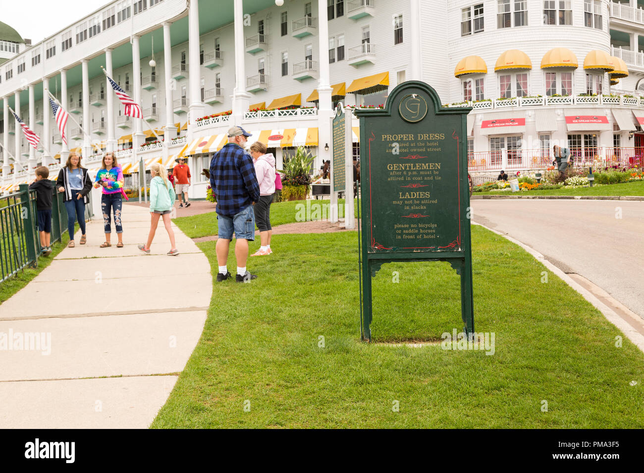 Outdoor sign with proper dress code rules, in front of the Grand Hotel resort on Mackinac Island, Michigan. The tourists  around are dressed casually. Stock Photo