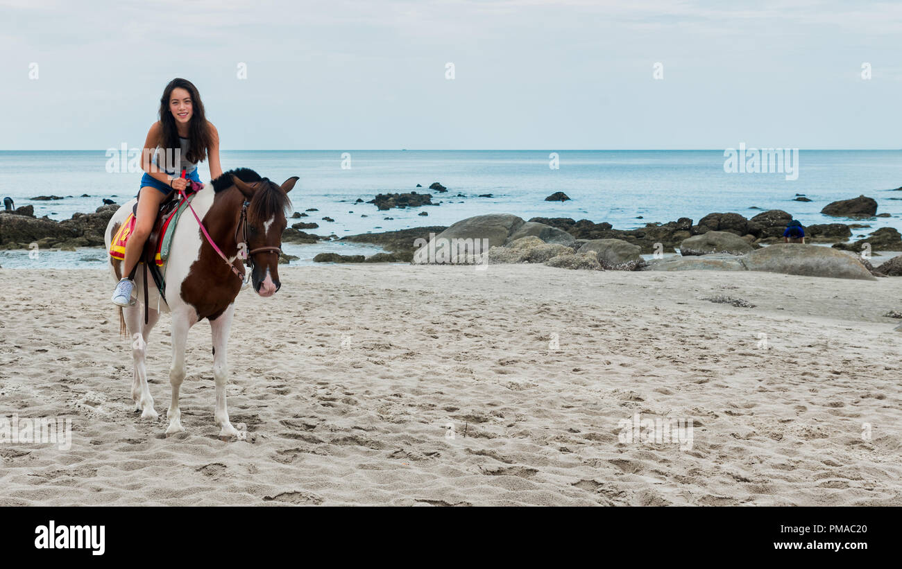 Young girl riding a horse on the beach in Hua Hin Thailand Stock Photo