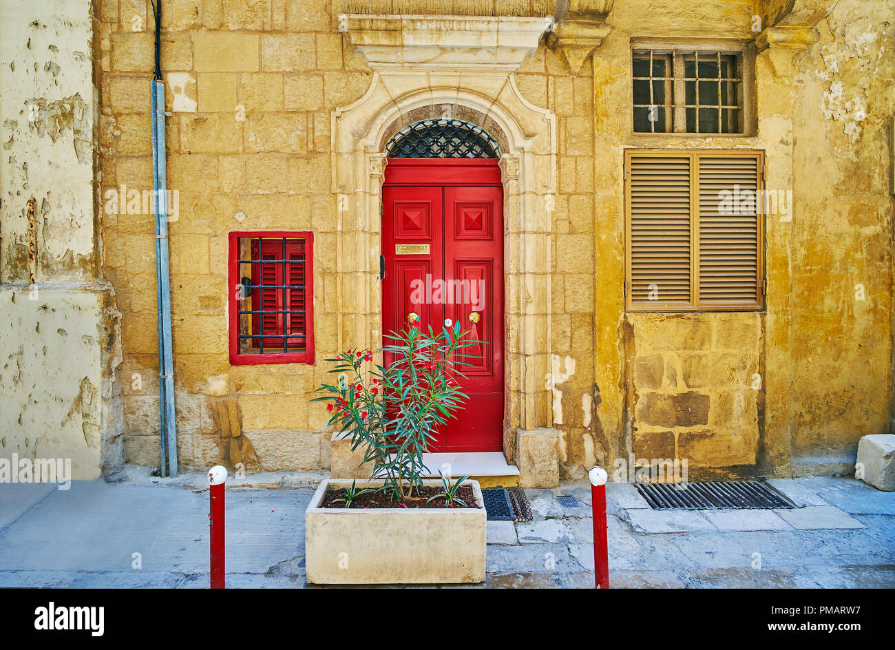 The old stone edifice decorated with wooden bright red door with relief doorframe, St Ursula street, Valletta, Malta. Stock Photo