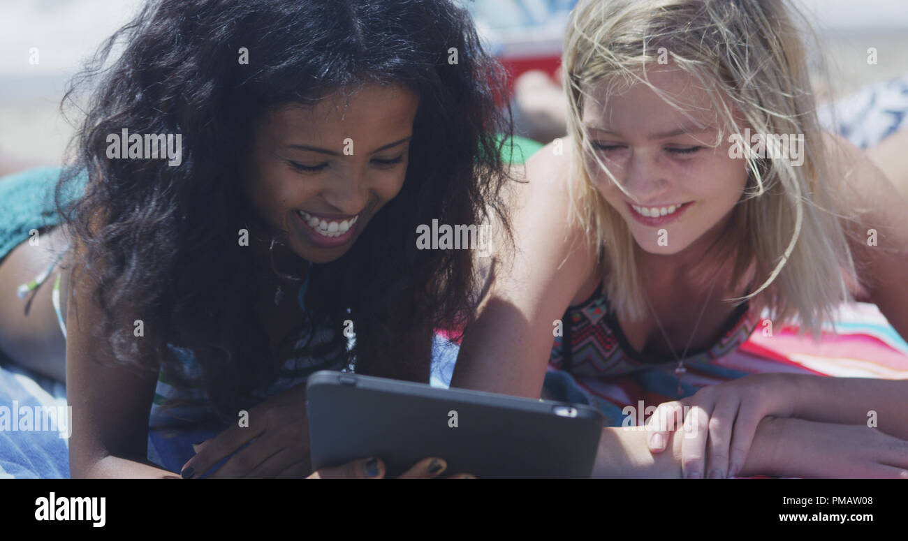Happy group of young interracial friends looking at tech on the beach Stock Photo