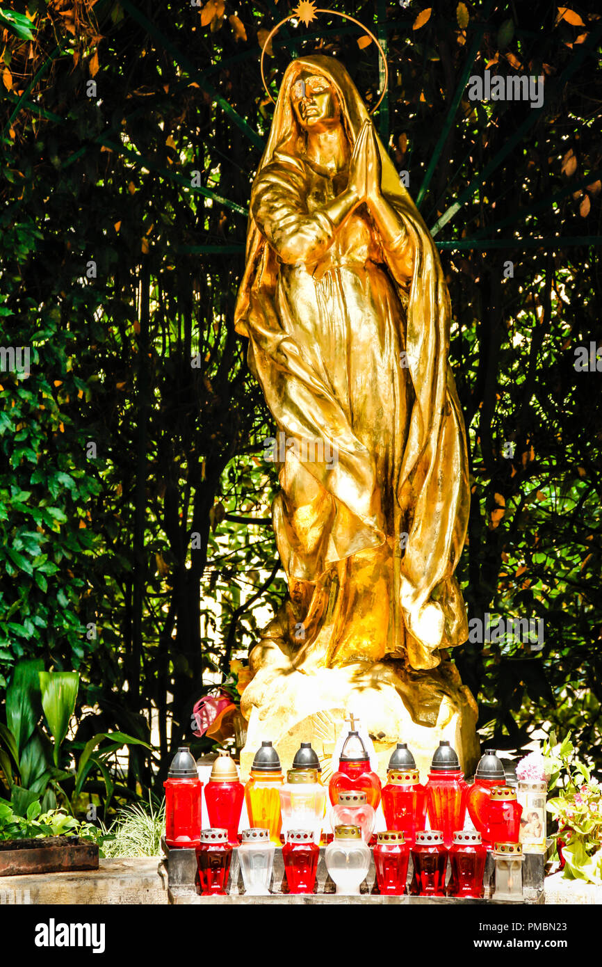 The gilded statue of Madonna in front of St Jacob's Church in Opatija, Croatia with beautiful cardholders in red glass Stock Photo