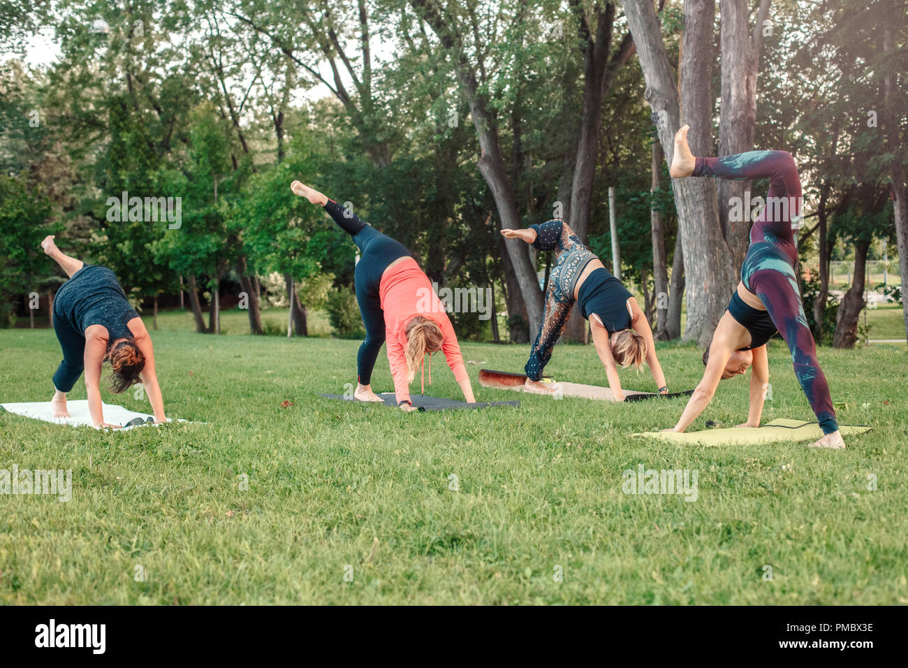 Group of many Caucasian people doing yoga in park outside on sunset ...