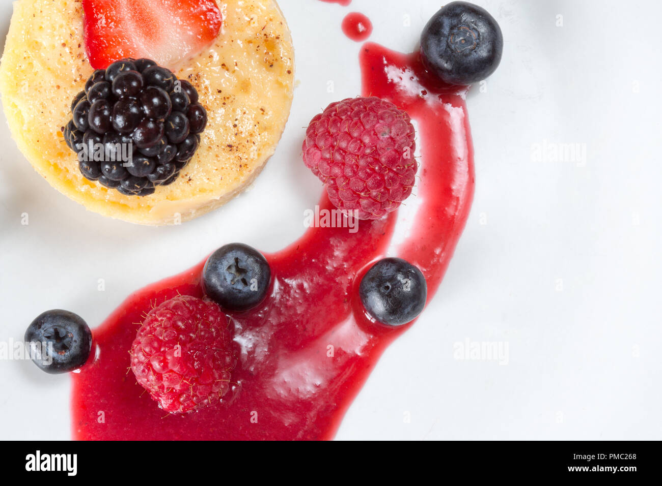 A serving of Egg custard tart with fresh strawberry, Raspberry and Blueberries with a raspberry coulis Stock Photo