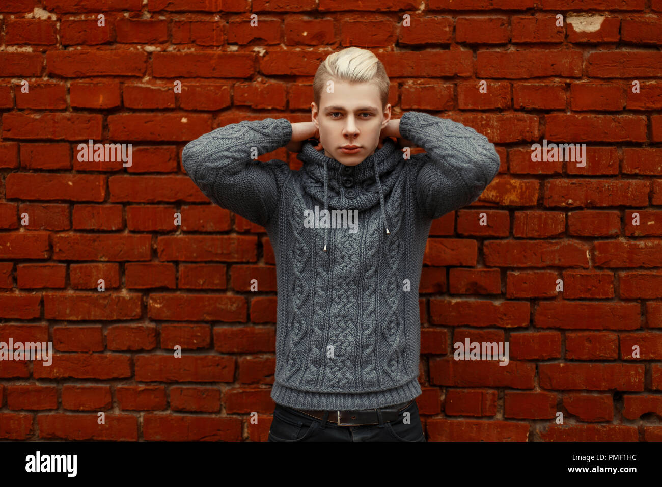 Handsome young man in trendy knitted sweater posing near brick wall Stock Photo