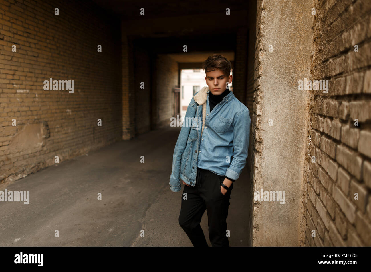 Stylish handsome man in a denim shirt with a trendy denim jacket posing outside near a brick wall Stock Photo