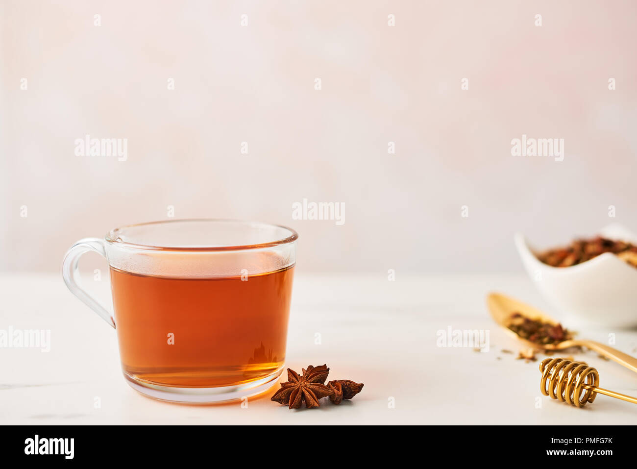 Black tea in a glass cup with golden spoon with herbs, dipper and anise on marble table top. Feminine rose background with copy space. Narrow depth of Stock Photo