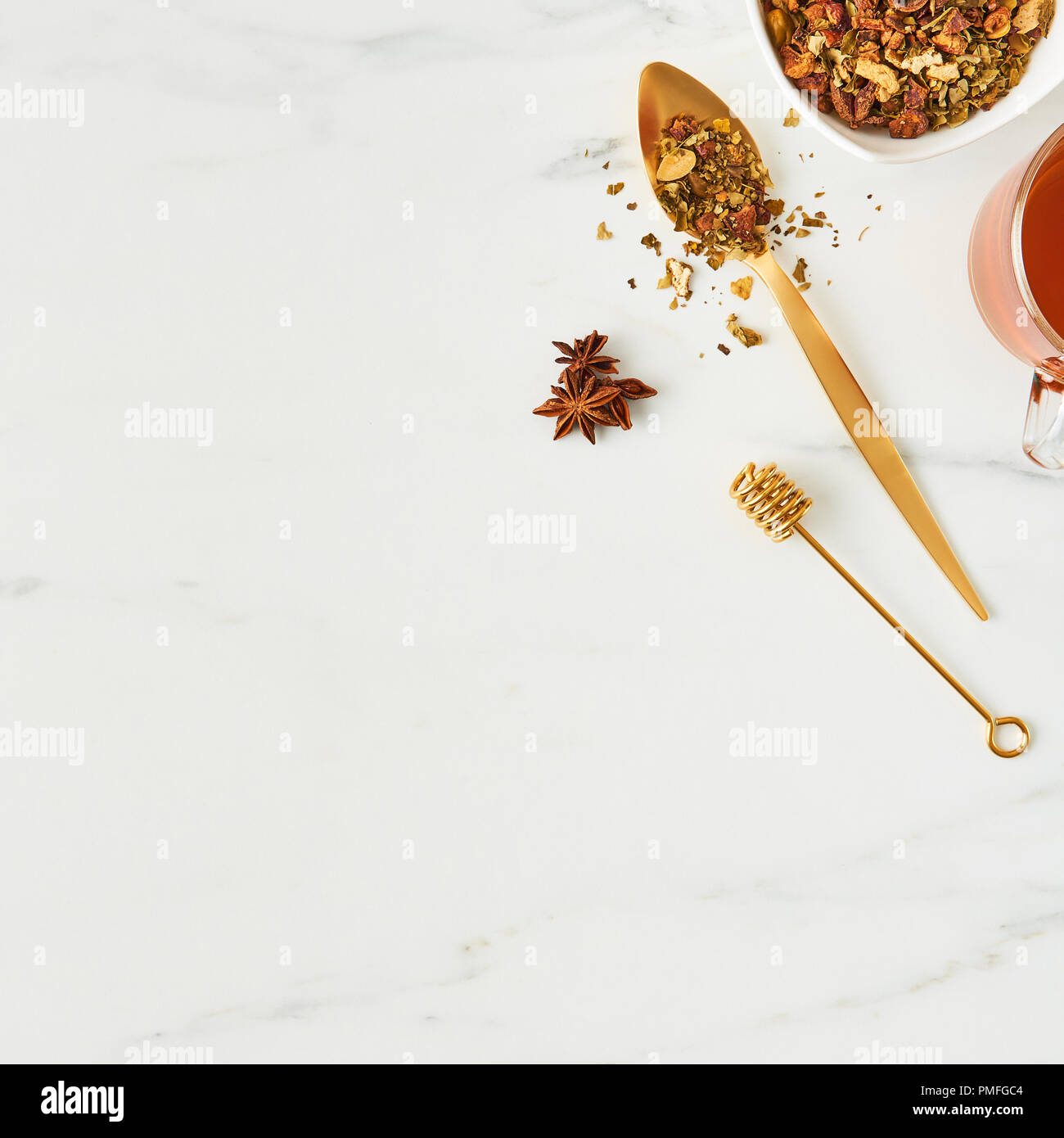 Flat lay of fresh black tea, with golden spoon, dipper and herbs on white marble background. Top view, square crop with copy space. Stock Photo