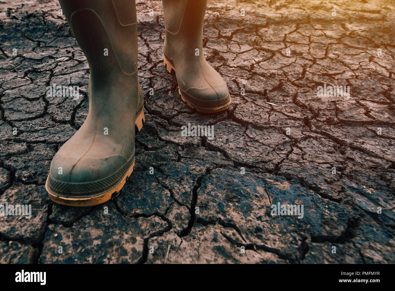 Farmer in rubber boots walking on dry soil ground, global warming and climate change is impacting crops growing and yield Stock Photo