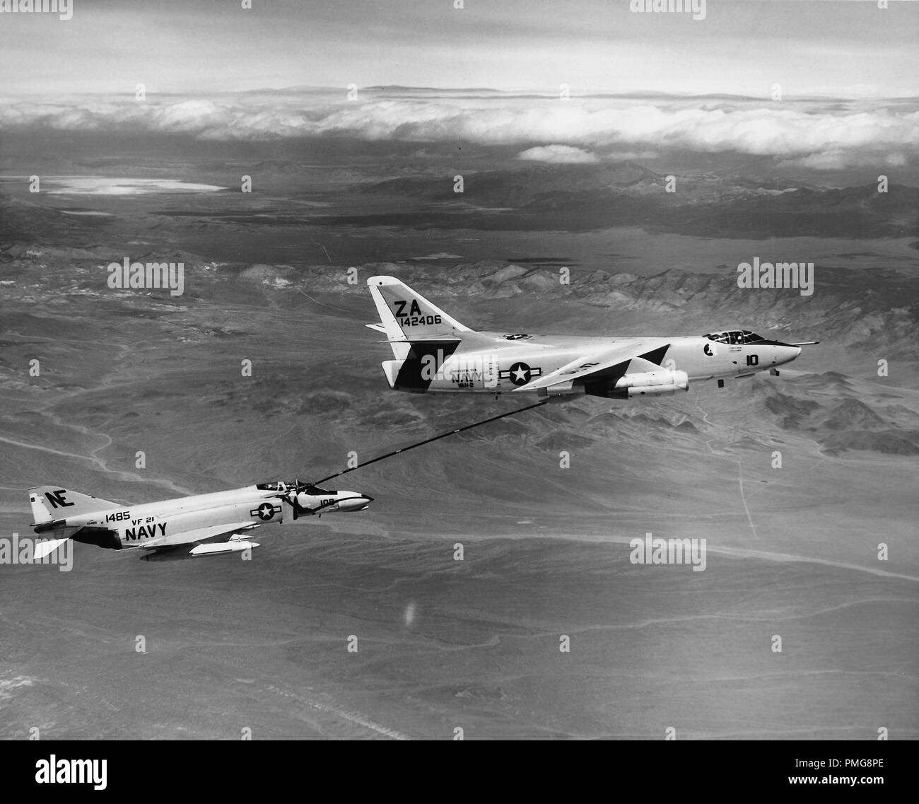 Black and white aerial photograph showing a pair of United States Navy aircraft, McDonnell Douglas F-4 Phantom IIs, refueling while in flight, with clouds and mountains in the distance, photographed during the Vietnam War, 1965. () Stock Photo