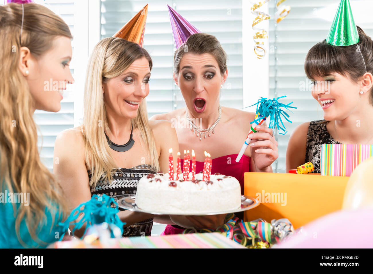Woman blowing out candles on her birthday cake while celebrating Stock Photo