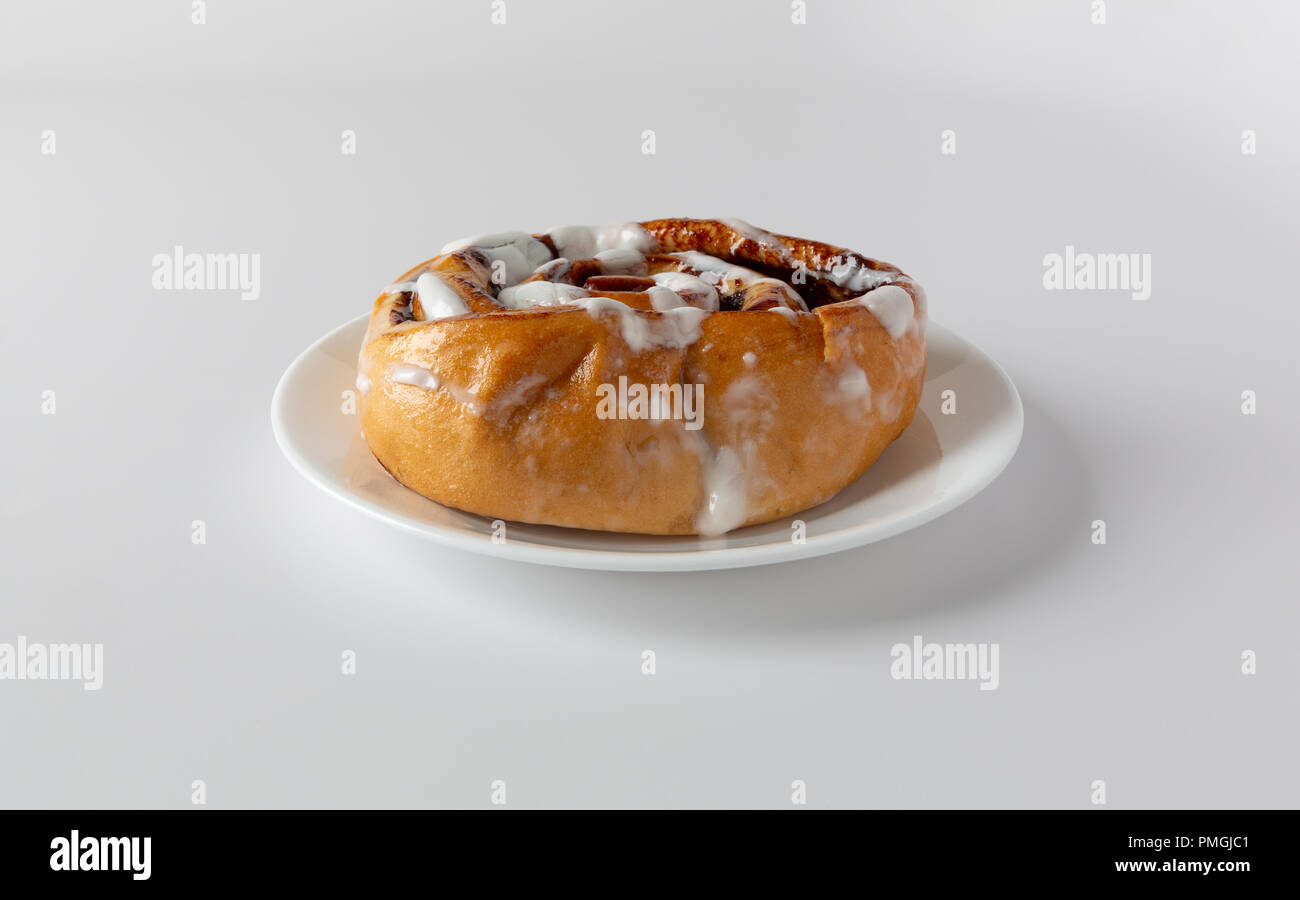 Side view of a warm, freshly baked cinnamon roll on plate atop a white ...