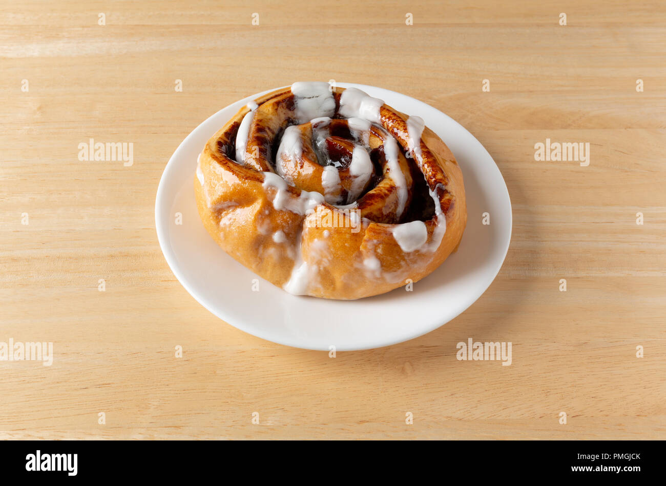 Side view of a freshly baked cinnamon roll on white plate atop a wood ...