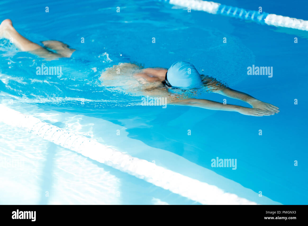 Photo of sporty man in blue cap floating on path in pool Stock Photo