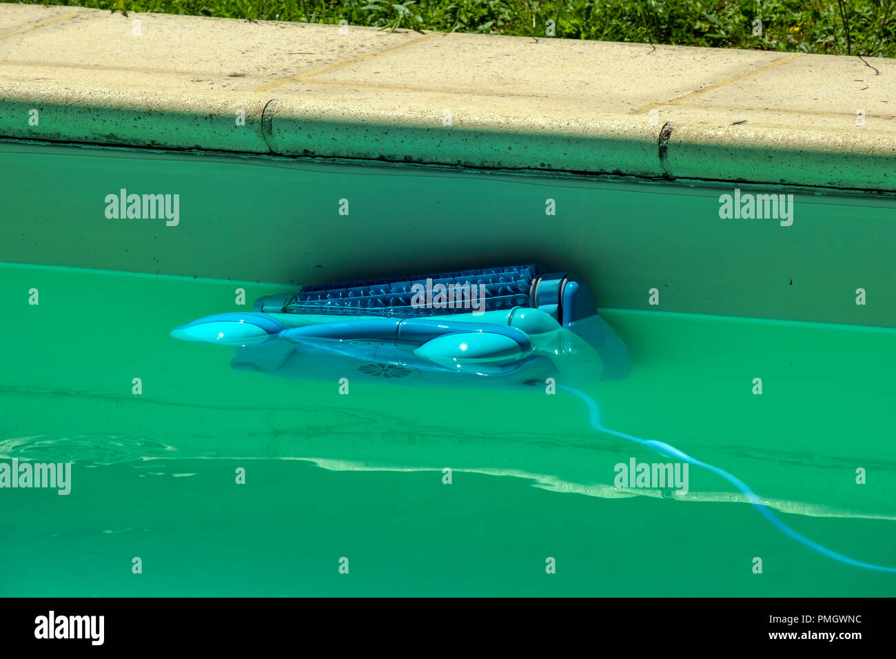 An automatic robot pool cleaner climbs the side of a cloudy swimming