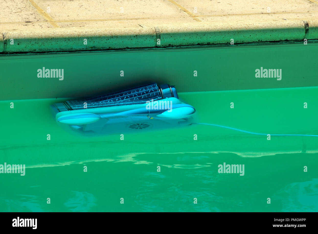 An automatic robot pool cleaner climbs the side of a cloudy swimming pool removing debris and algae Stock Photo