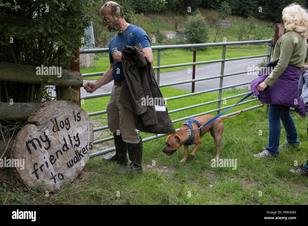 Country walkers pass through a gate with their dog, next to a sign reassuring those entering a field that a pet nearby is walker-friendly, on 10th September 2018, near Lingen, Herefordshire, England UK. Stock Photo