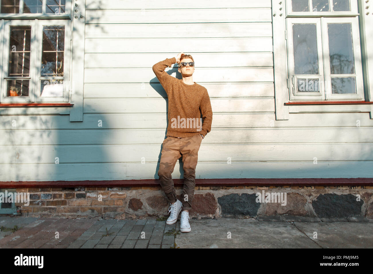 Stylish beautiful young man in fashionable spring clothes posing near a vintage house with windows Stock Photo