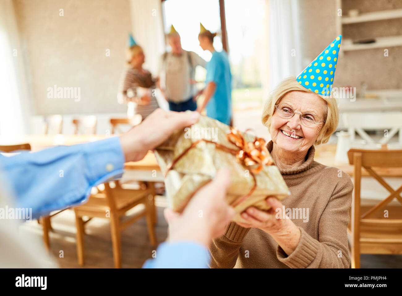 A senior as a birthday child is happy about a present at her birthday party Stock Photo