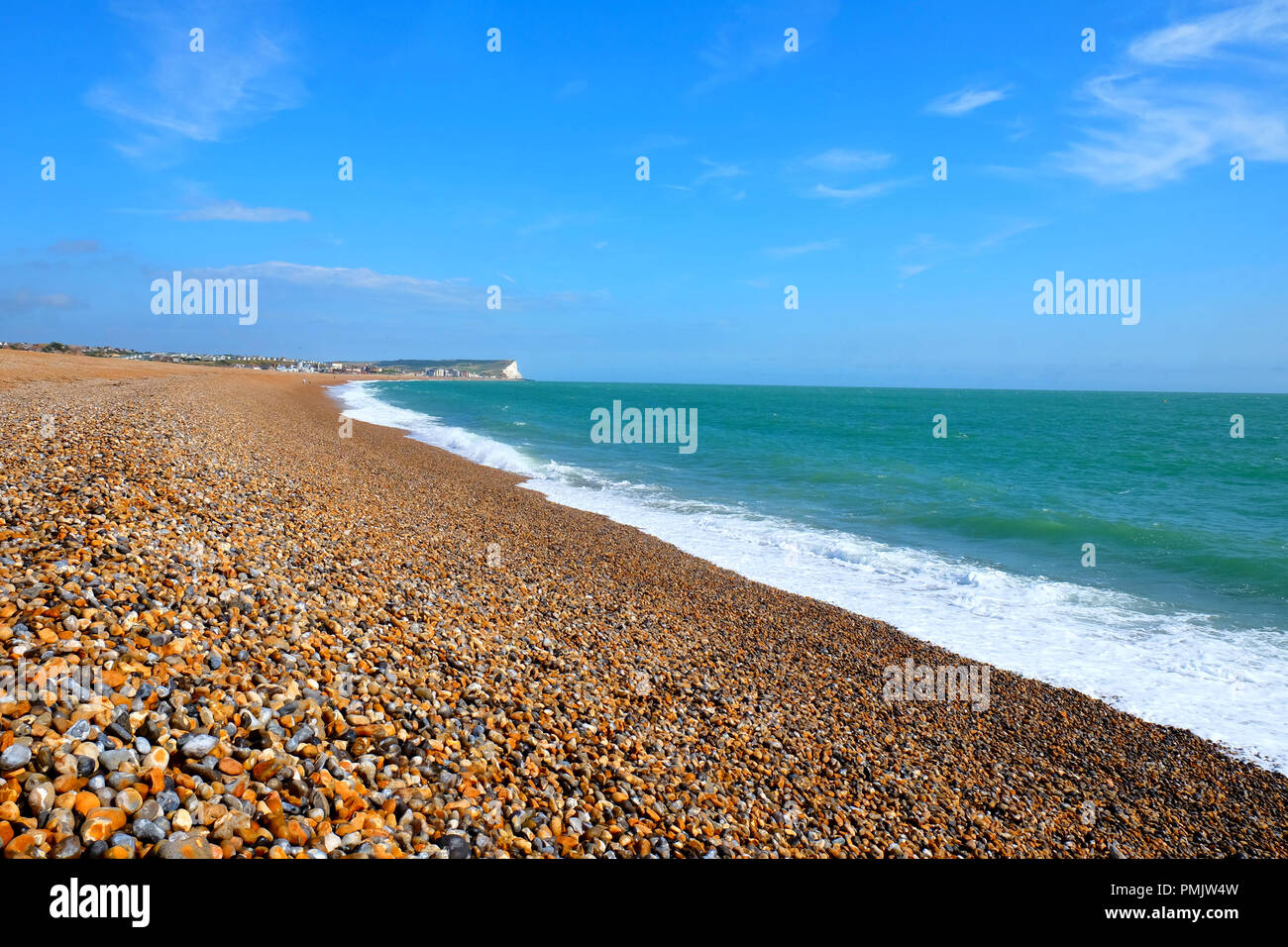 A bright sunny day the long sweeping curve of Seaford Beach East Sussex UK in the foreground is the pebble beach then the white of the breaking waves  Stock Photo