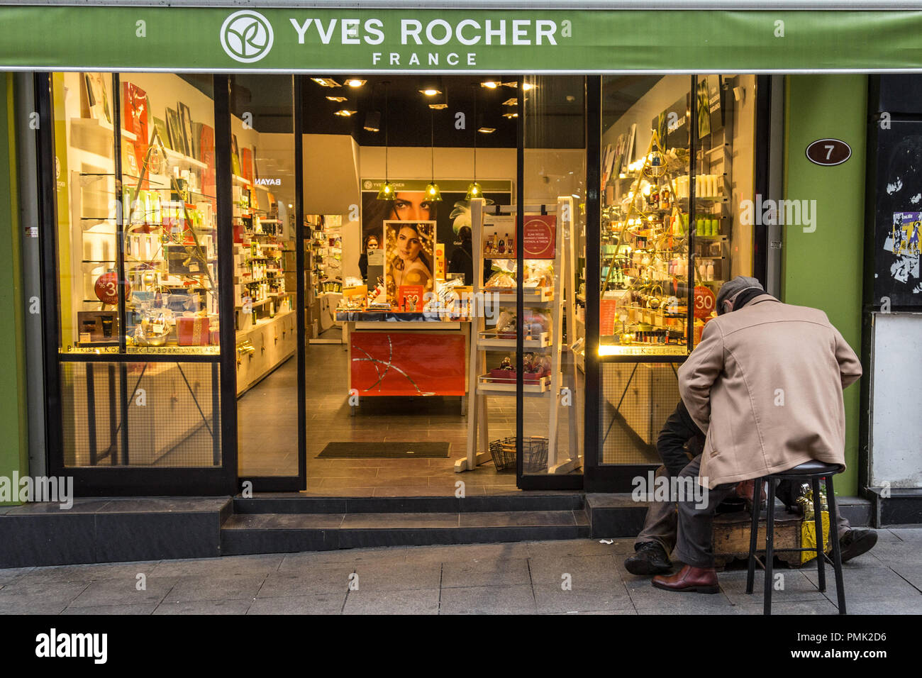 ISTANBUL, TURKEY - DECEMBER 29, 2015: Shoeshiner polishing shoes in front of the local Yves Rocher store with its sign. Yves Rocher is a French cosmet Stock Photo