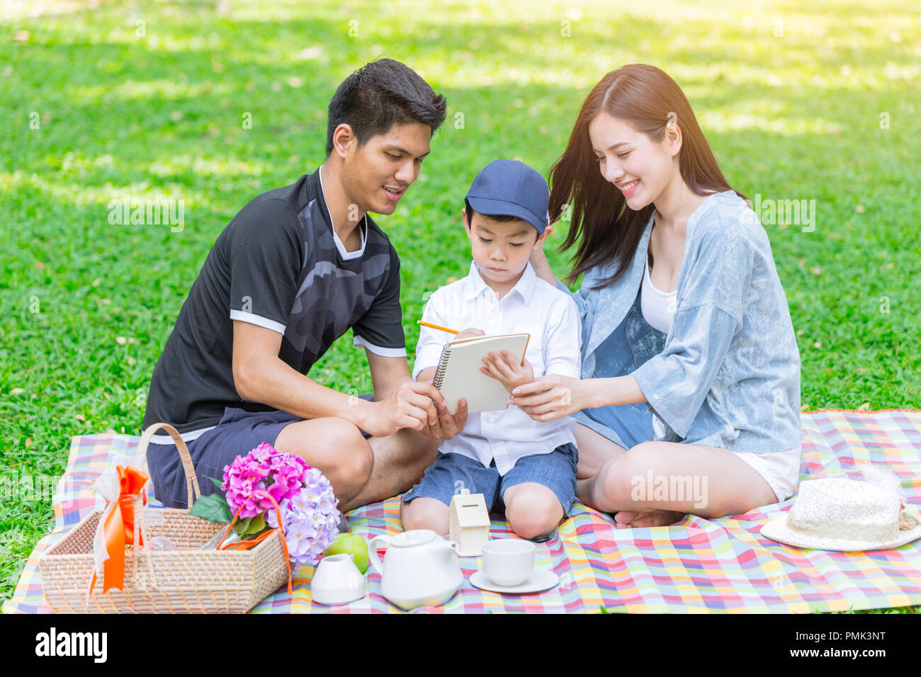 Asian teen family teaching son homework while picnic at outdoor park Stock Photo