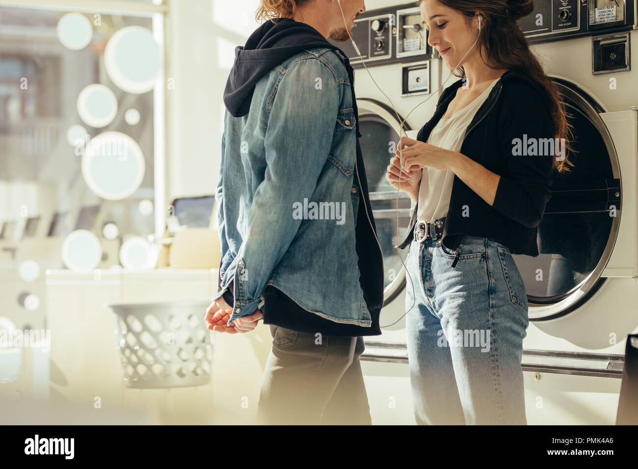 Couple Sharing Earphones Listening To Music Standing In A Laundry Room Couple In Love Standing