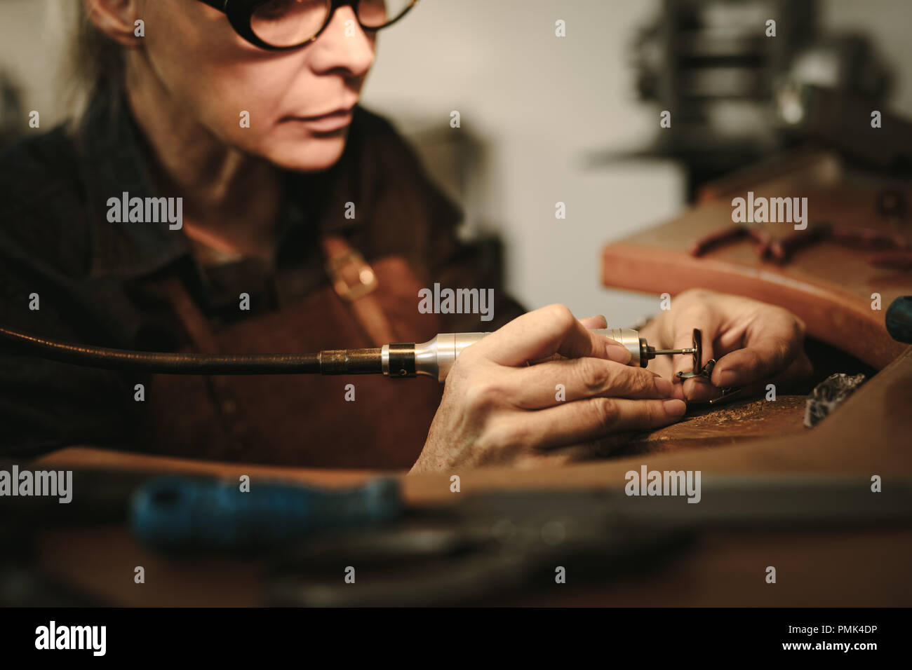 Senior female jewelry maker polishing a product at her workbench. Jewelry designer polishing a bracelet at workshop. Stock Photo