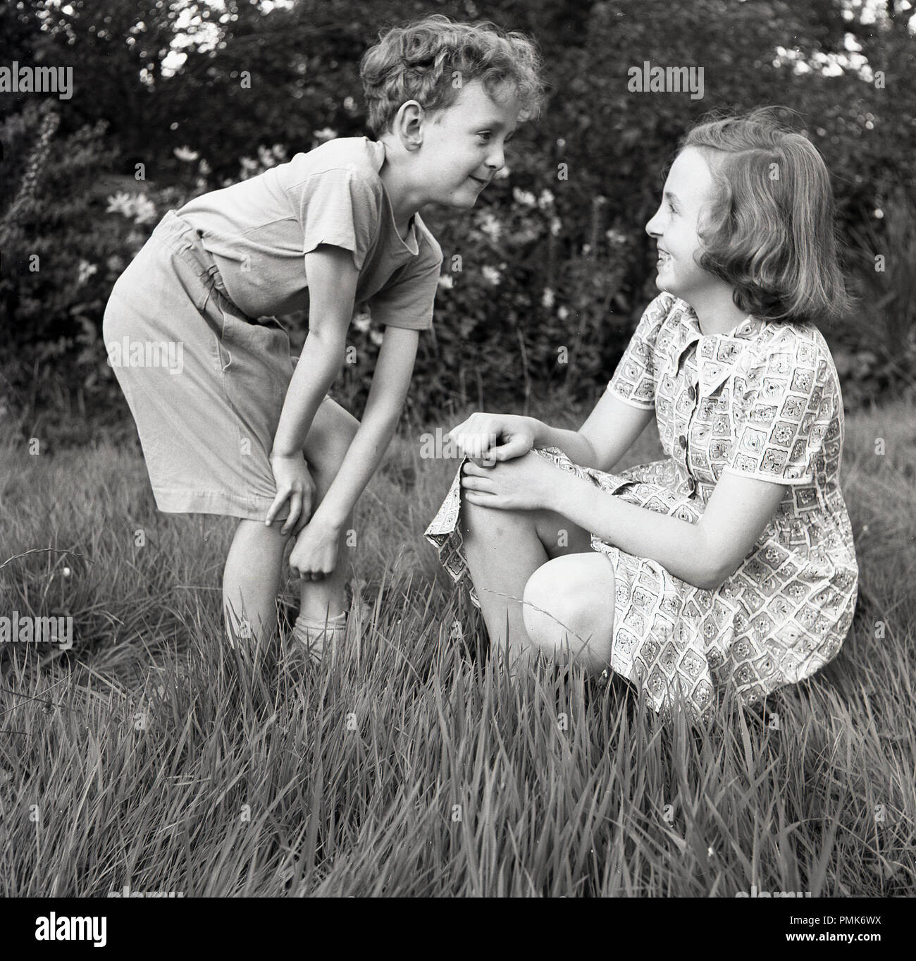1950s, historical, children playig keep a 'straight face' outside in the grass, big sister laughing at her younger brother''s 'funny' face, England, UK. Stock Photo